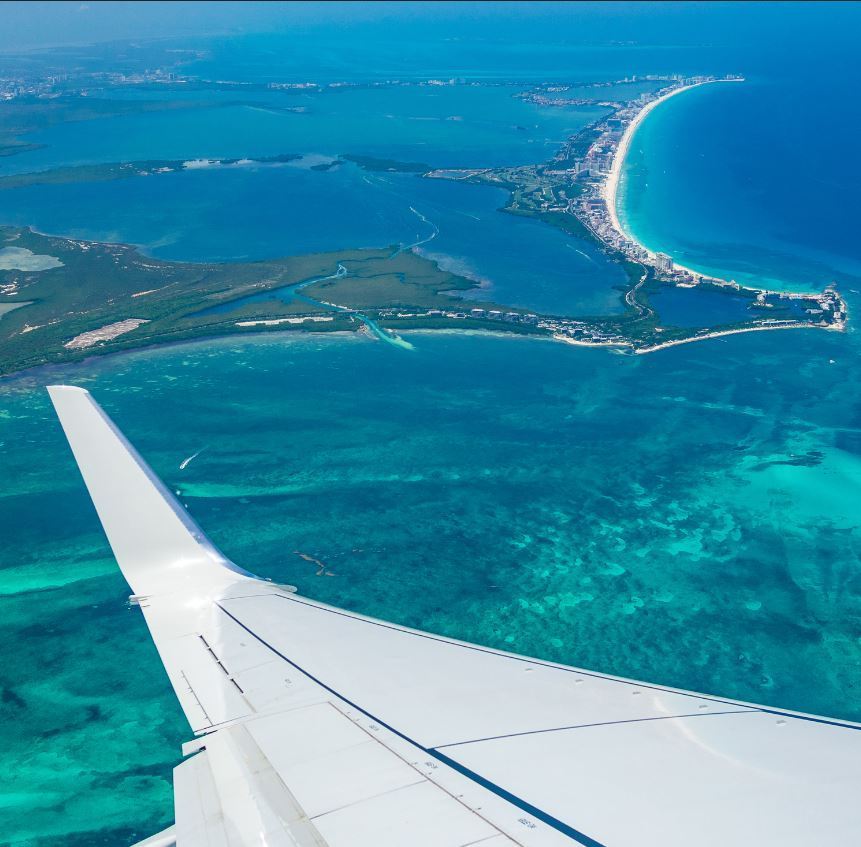 view of a wing of a plane flying over Cancun during the day.