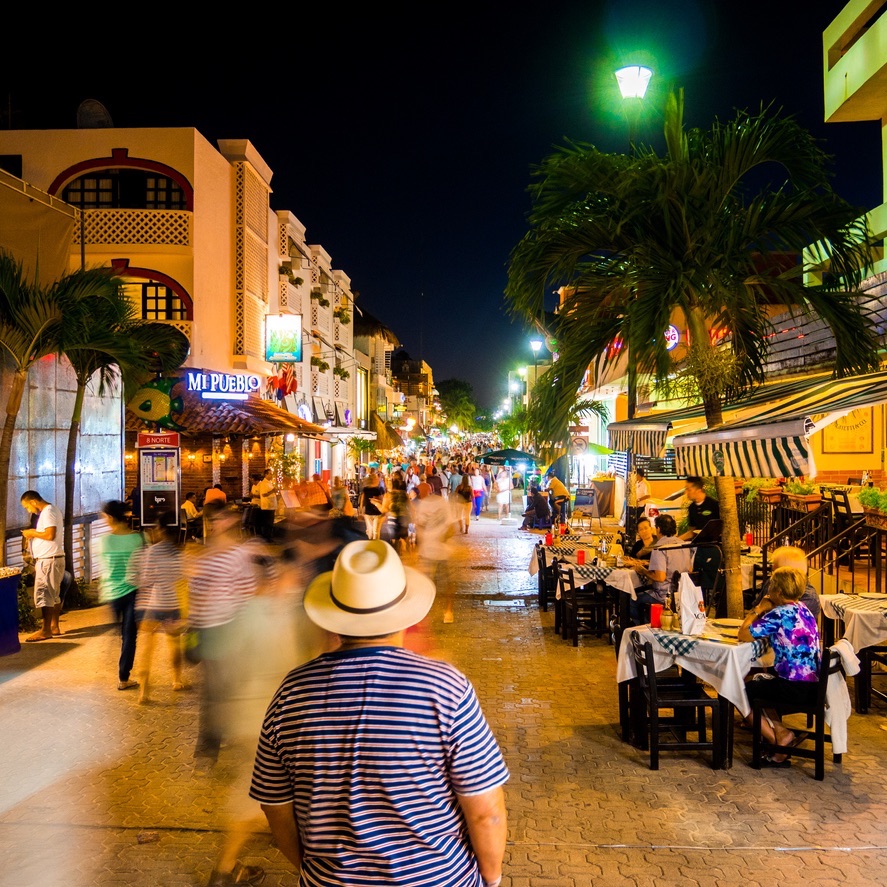 People walking around the lively Calle Quinta Avenida at night in Playa del Carmen, Mexico.