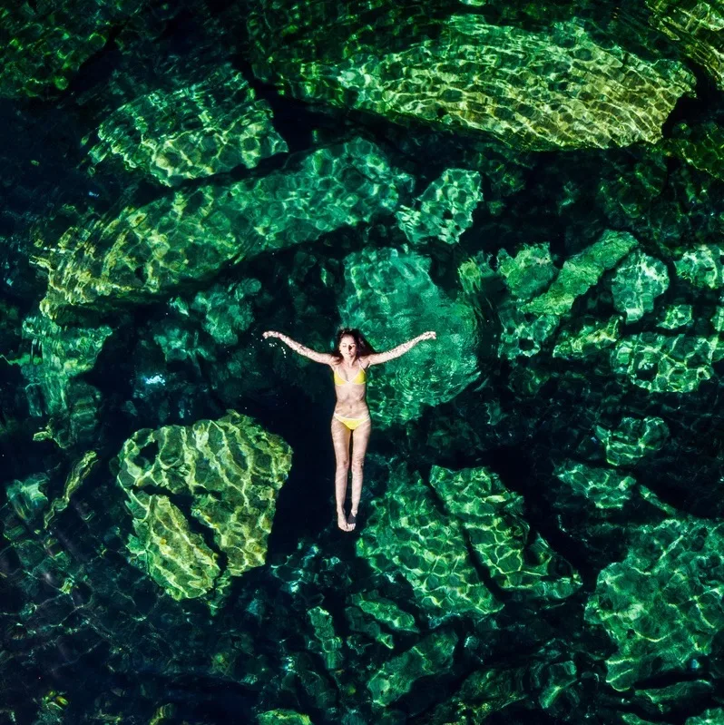 Overhead shot of a attractive young brunette woman in a bikini floating in the Cristalino cenote.