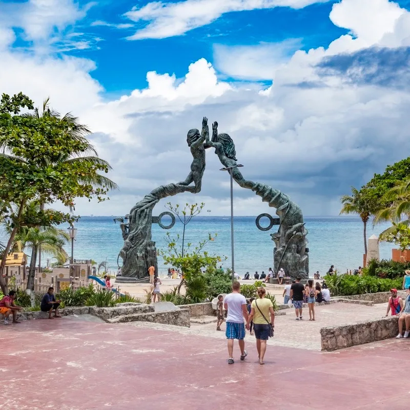 Tourists entering Parque Fundadores in Playa del Carmen with a view of the beach in the background.