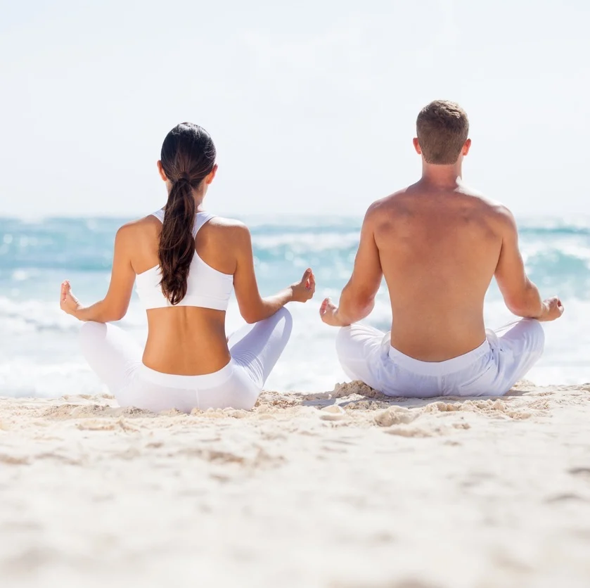 a couple doing yoga meditation on a beach
