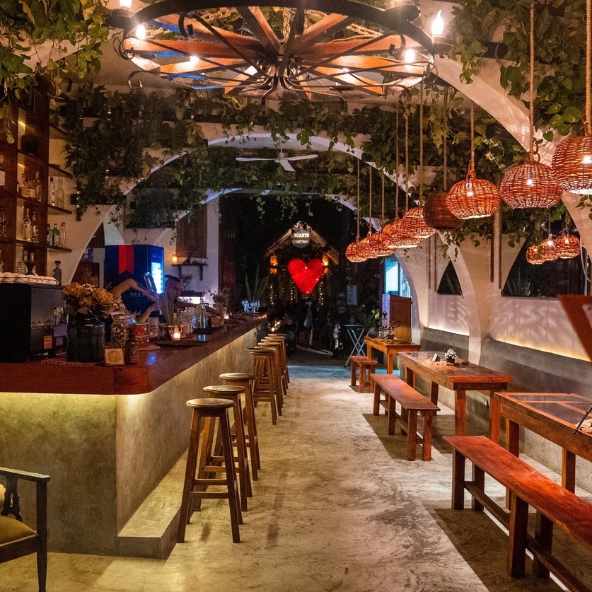 Famous decorated open air retro cafe in Tulum illuminated at night. Elegant decorated restaurant with place setting and bar counter.