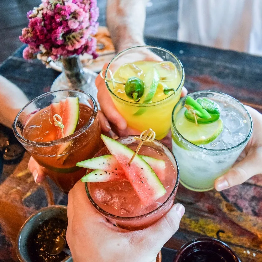 Friends toasting, saying cheers holding tropical blended fruit margaritas.  Watermelon and passionfruit drinks.