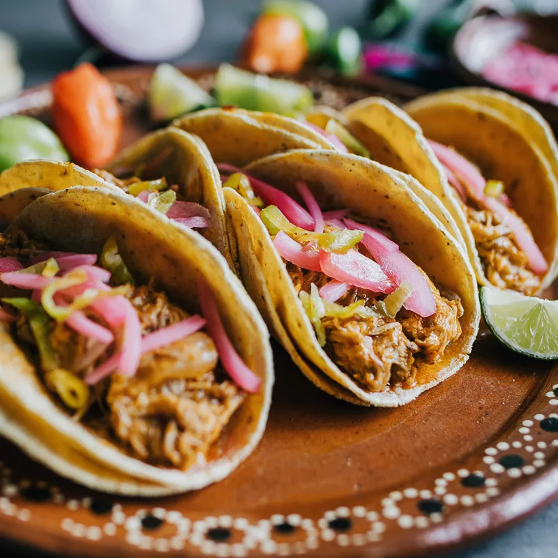 Plate full of tacos with meat and onions and a lime on the side.