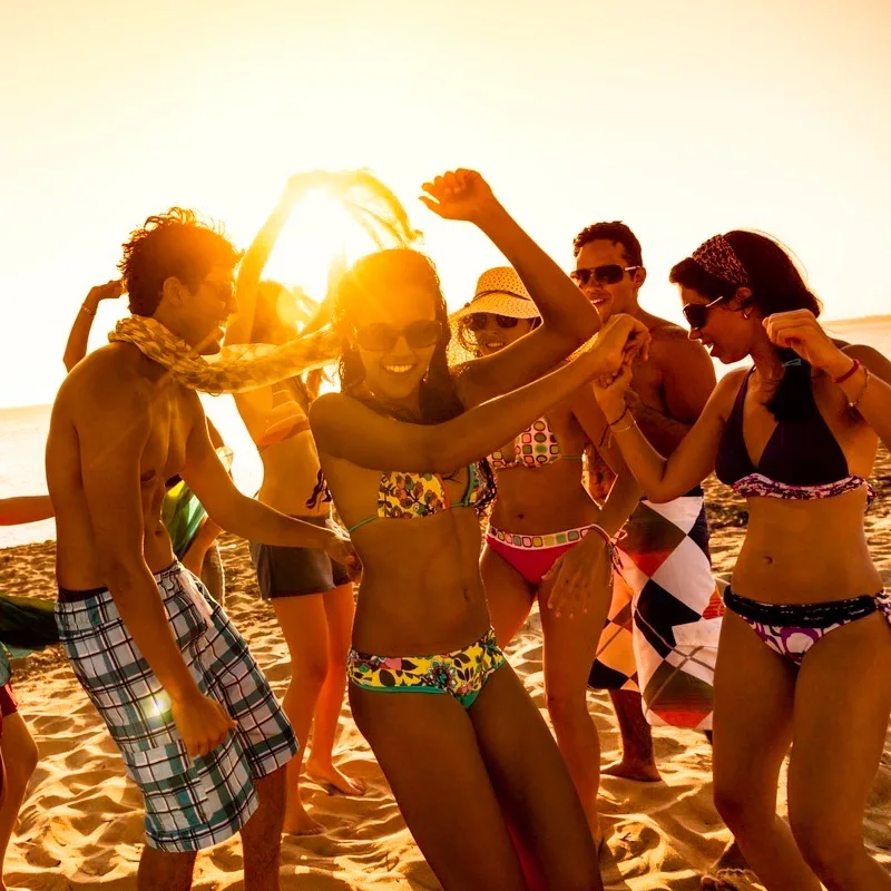 travelers dancing on a beach with a sunset in the background