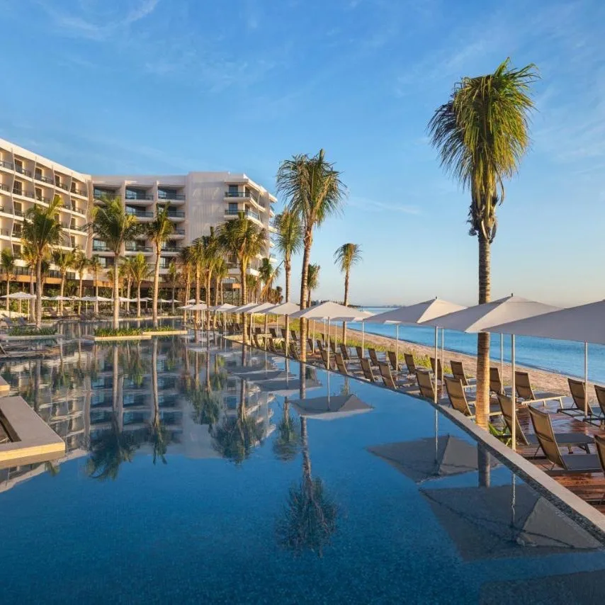 pool view of Hilton Cancun with clear skies and palm trees, overlooking the ocean
