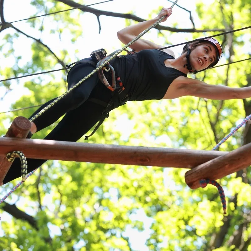 A woman climbing through a treetop adventure park