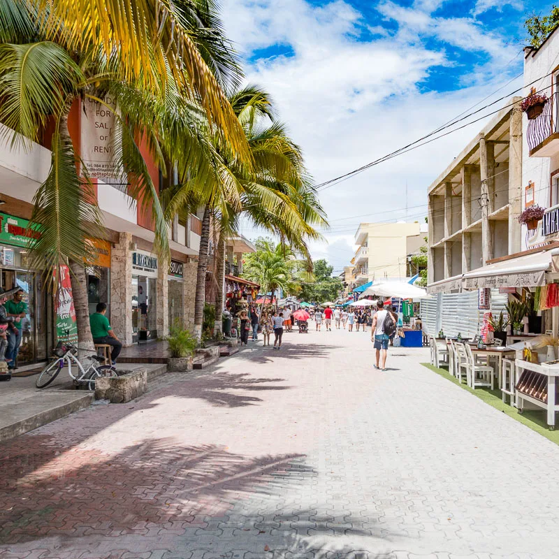 Cancun street filled with stores and restaurants and tourists walking around.