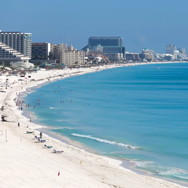 Cancun Hotel Zone and beach with tourists enjoying the sunshine and hotels in the background.