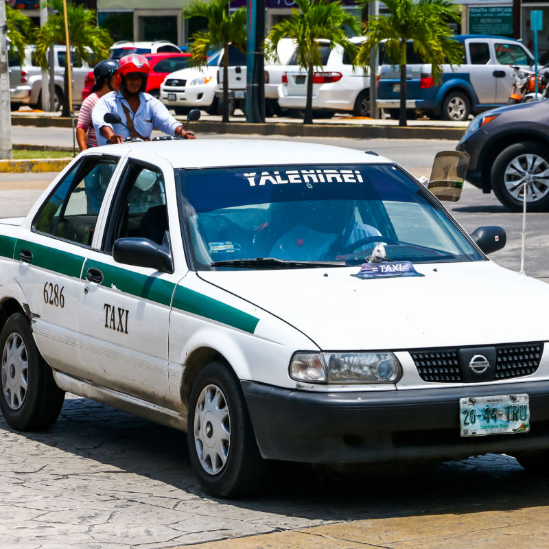 Cancun Taxi driving down the street with a man and woman on a bike behind the vehicle.