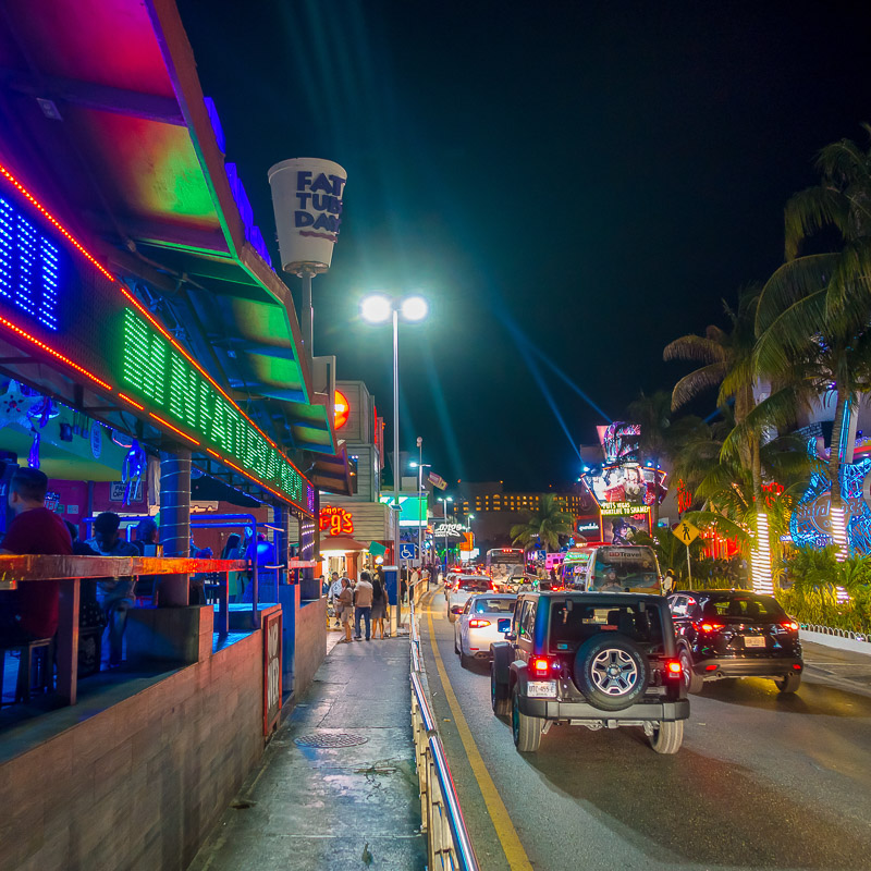 Cars and people on a street in Cancun, Mexico at night.