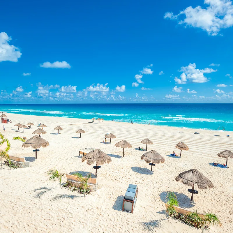 Cancun beach with tourists sitting under umbrellas and looking at the aqua blue water.