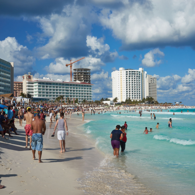 Tourists on a beach in Cancun, with hotels in the background.