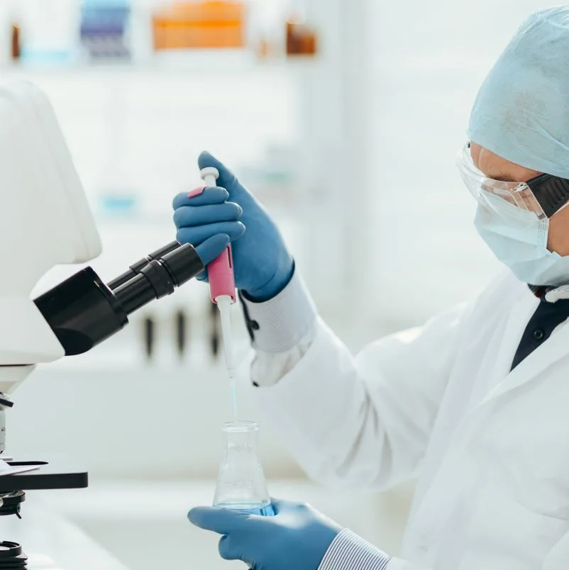 Medical researcher testing some form of liquid while wearing gloves and a mask.