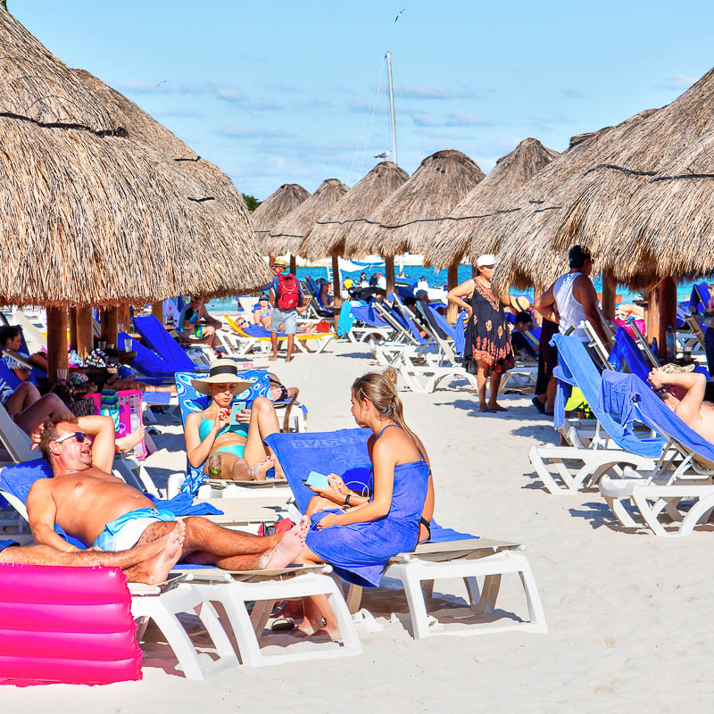 Busy Cancun beach with tourists sitting on lounge chairs and enjoying the warm weather.