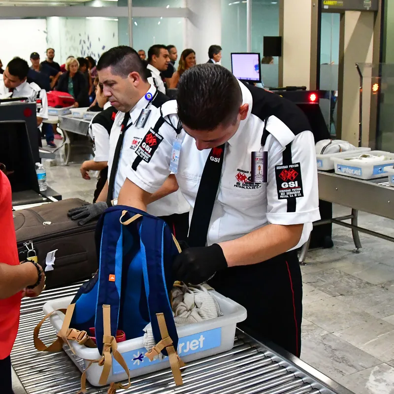 Airport security going through someone's bags while the passenger waits off to the side.