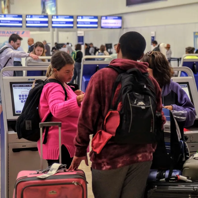 Tourists at Cancun Airport checking in and looking at phone.