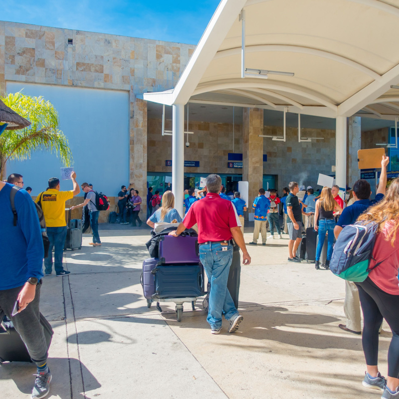 tourists and passengers waiting outside with their luggage at Cancun International airport during the day
