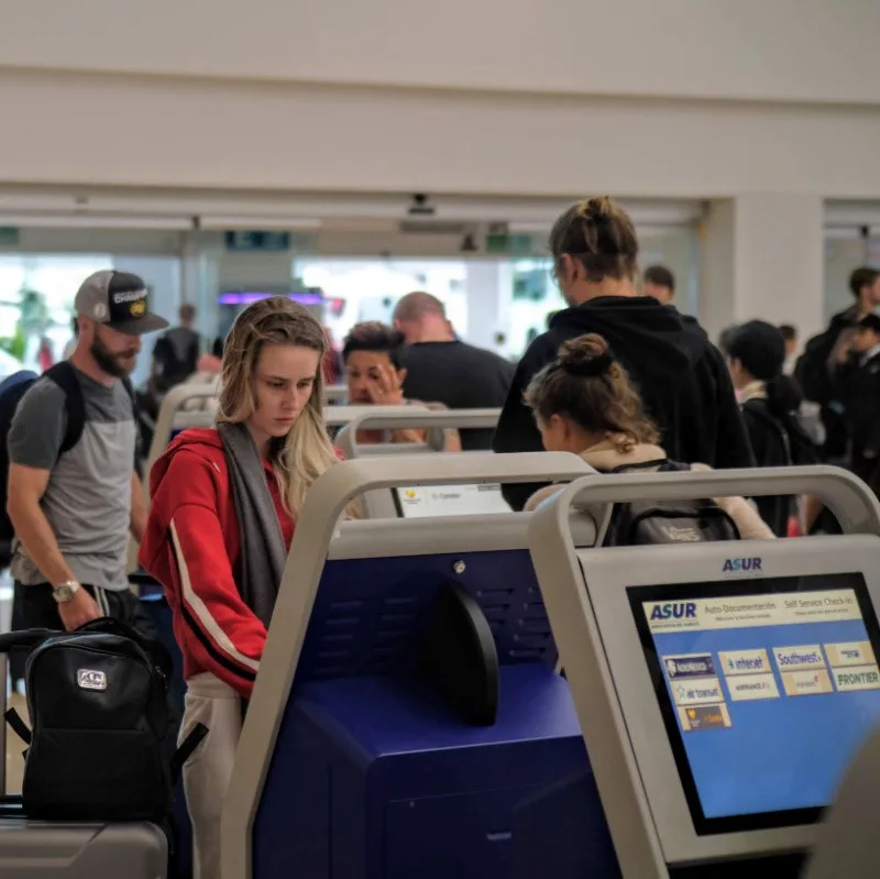 tourists at kiosks checking into their flights at Cancun Airport.