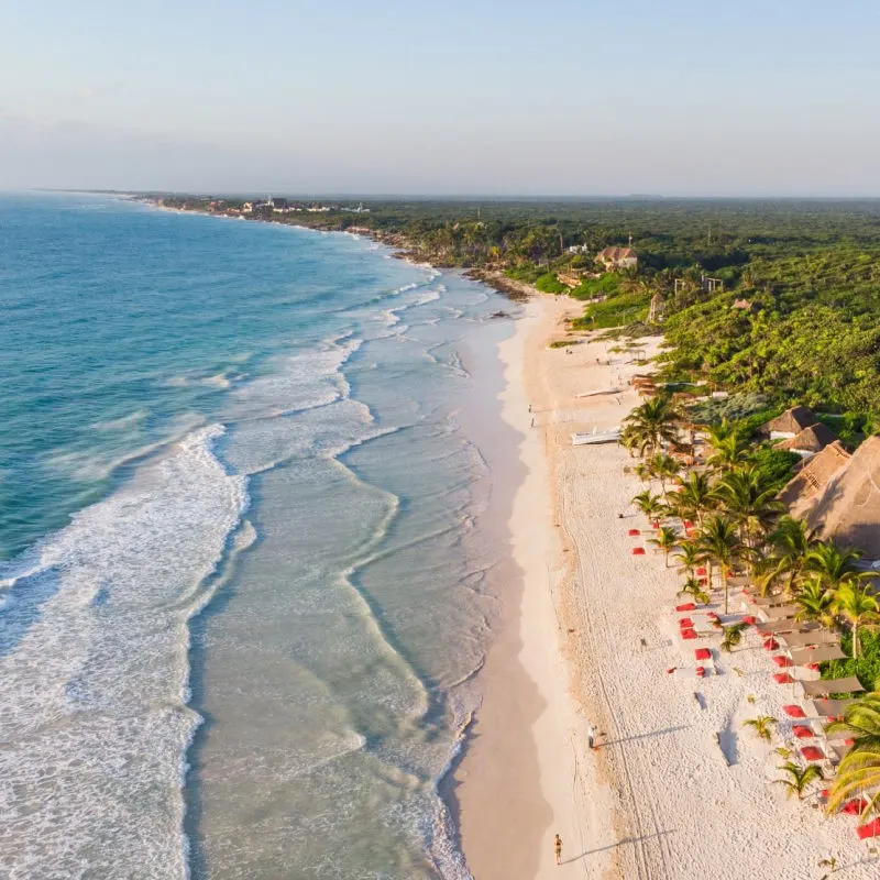 birds eye view of a picture perfect Beach in Tulum during the day, before sunset. red beach umbrellas scattered along the beach. 