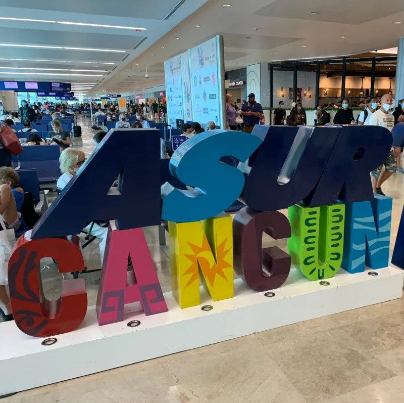 Cancun International Airport sign with people and shops in the background.