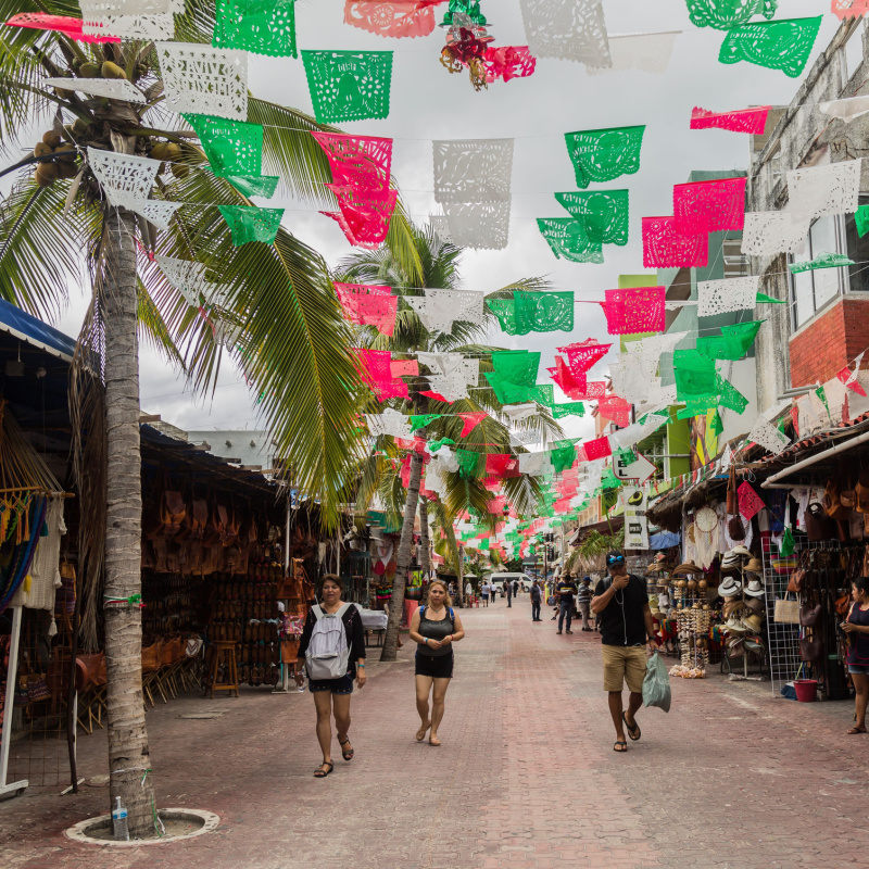 tourists walking on 5th avenue, papel picado white, green, and red flags waving above. 