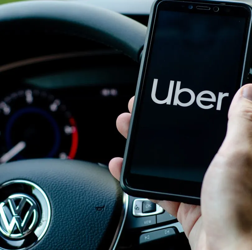 close up of hand holding a phon with the Uber app open. steering wheel in background.