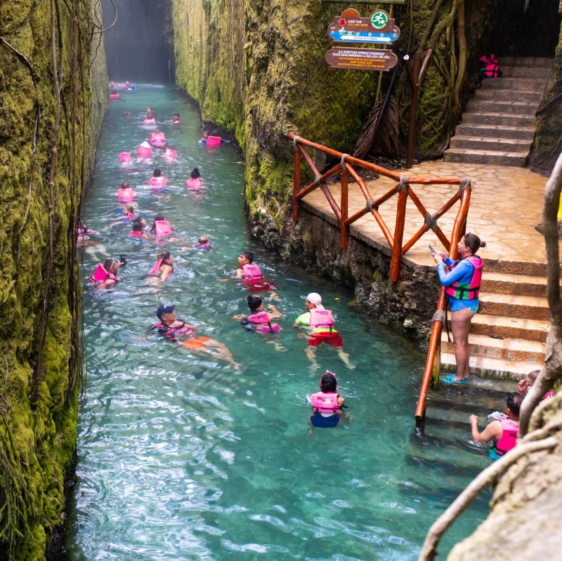 Xcaret Underground River with people swimming in the water and standing on the stairs.
