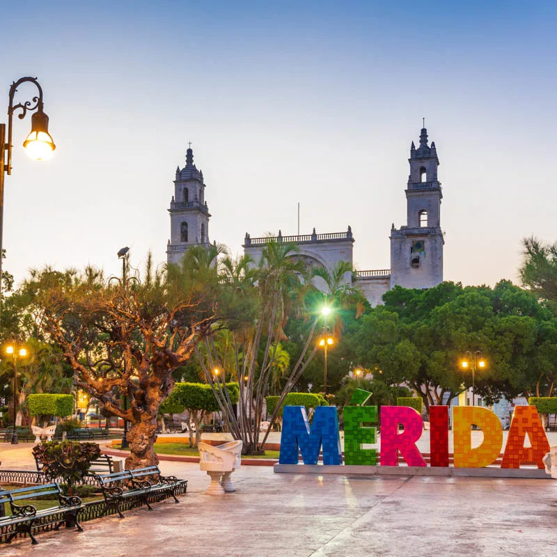 Merida central square and sign with benches off to the side and beautiful greenery.