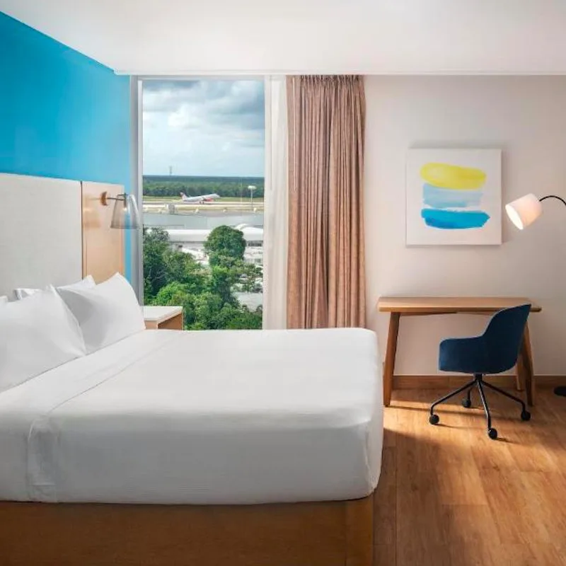 hotel room with white bed and view of airport during the day at Hilton Garden Inn Cancun Airport