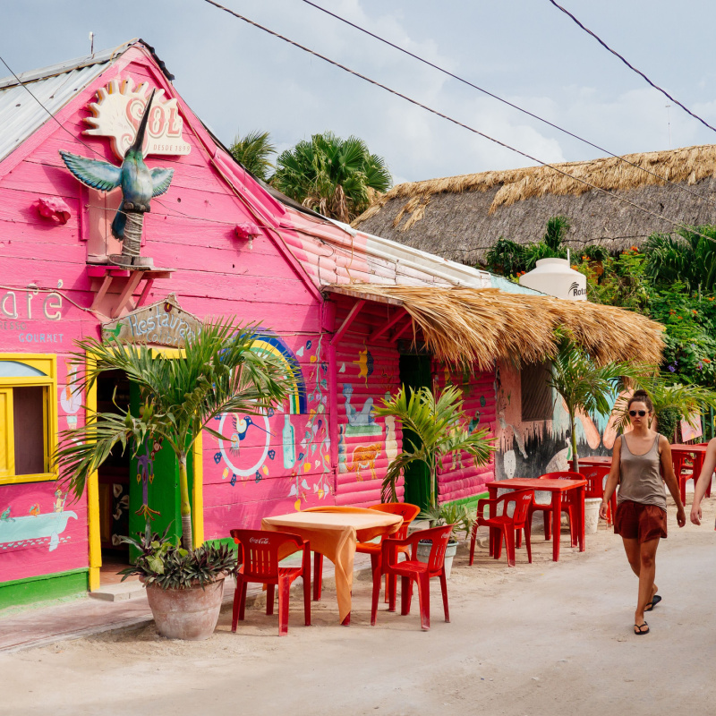 tourists walking on a main road in Holbox in front of a pink colored restaurant