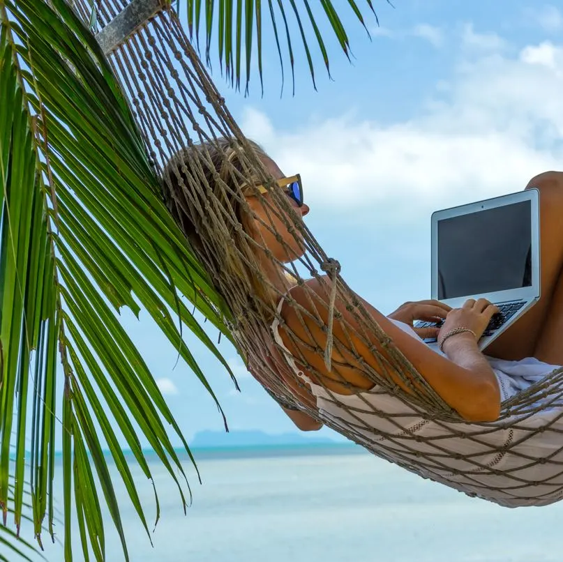 Woman working on laptop in hammock on beach