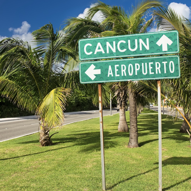 cancun airport sign outside by the highway, palm trees in the background.