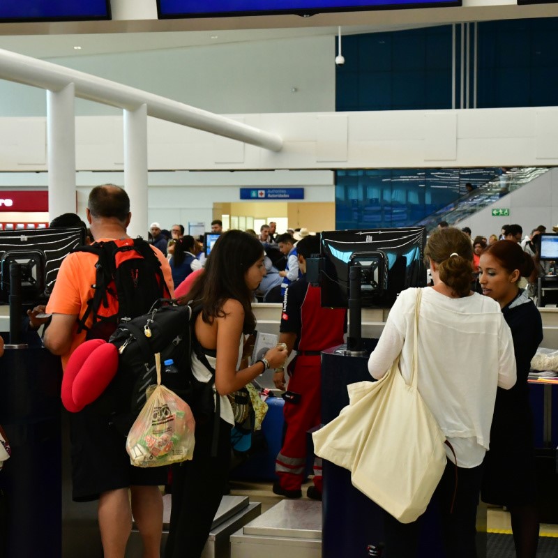 Busy Cancun International  Airport filled with travelers and their luggage.