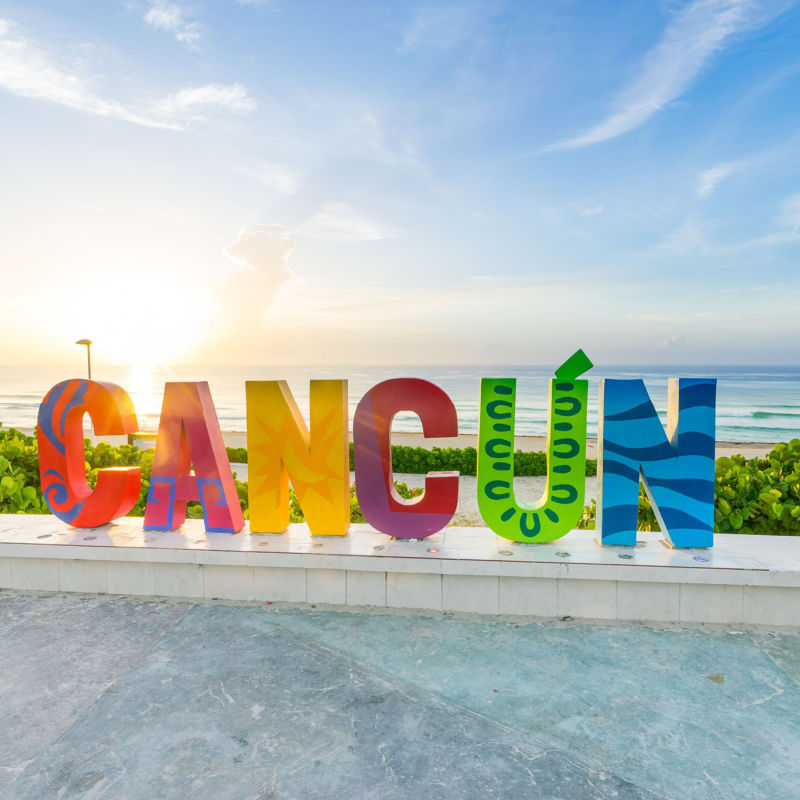 Cancun sign in front of a beach at sunset