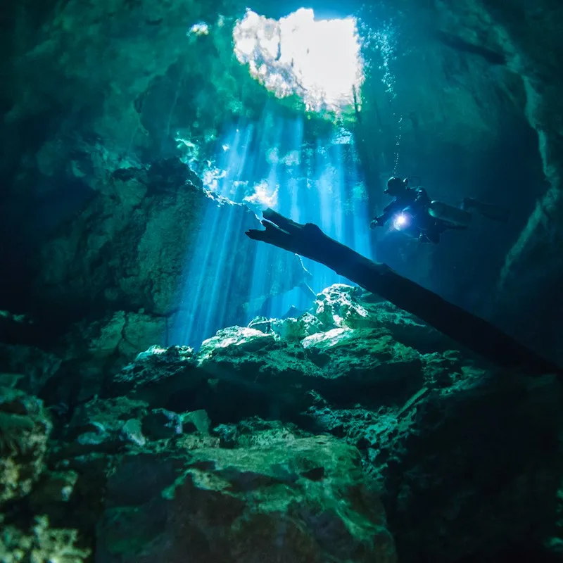 diver underwater in Cenote Tajma Ha near Cancun, cave opening and light above.