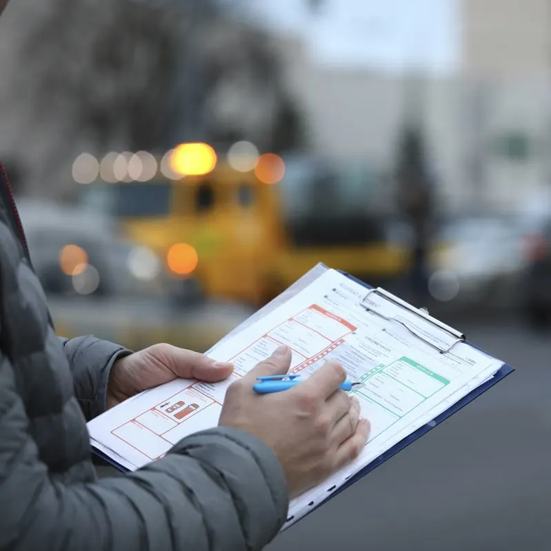 Close-up of male's hand filling report claim form on clipboard outdoors