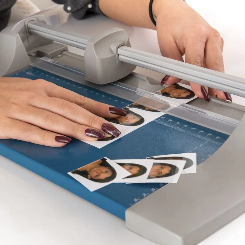Woman cutting and sizing passport photos in a photographic studio on a small portable guillotine in a close up view of her hands