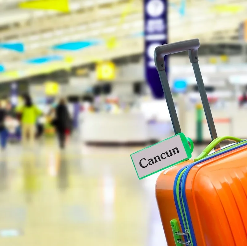 orange wheelie suitcase with tag marked Cancun at the airport.