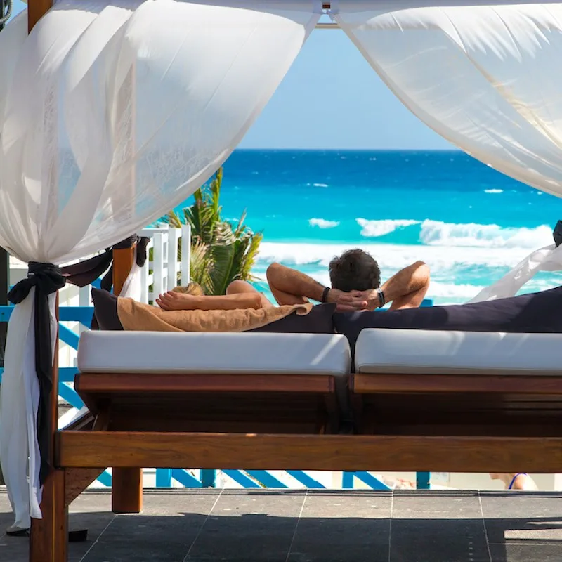 Sun beds facing to the caribbean sea in Grand Pyramid hotel in Cancun. People chilling out by the water and looking on the beach.