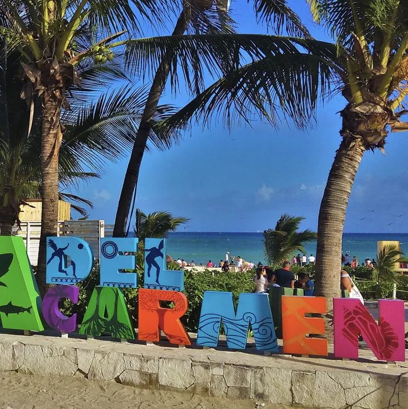 playa del carmen sign by the water and palm trees and crowd