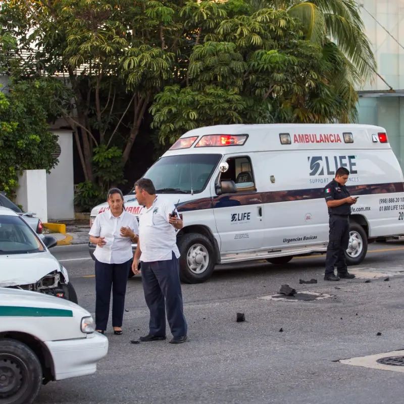 Accident in Cancun with an ambulance in the background with a driver standing in front of the vehicle and two people talking on the street.
