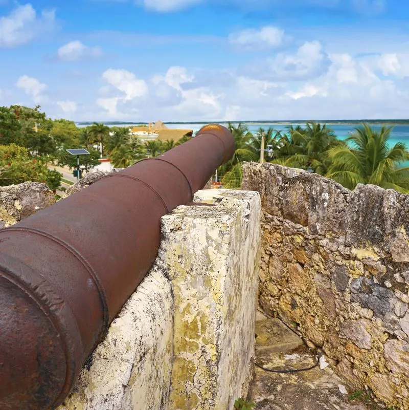 old cannon at San Felipe fort with blue water and palm trees  in Bacalar Quintana Roo of Mexico 