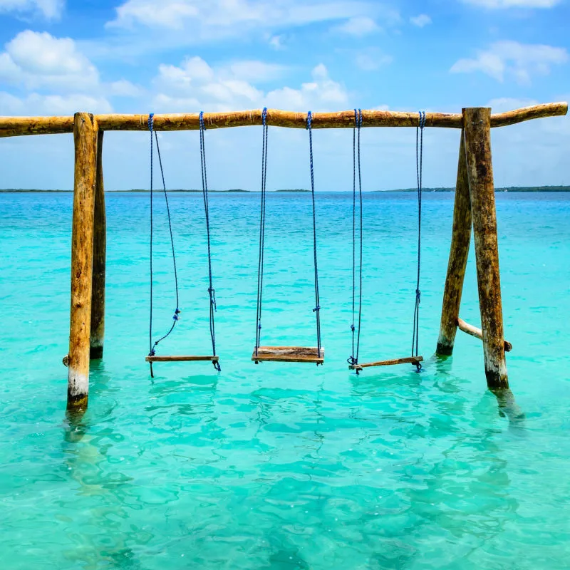 A wooden swing in a Bacalar beach with colourful water