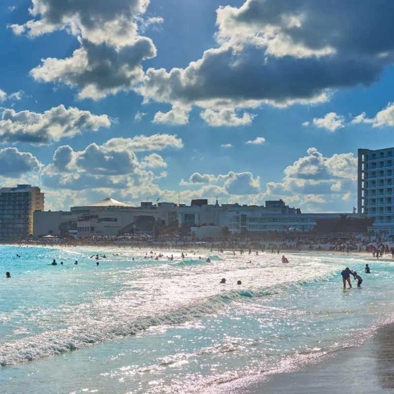 Beach in Cancun Hotel Zone with people swimming in the water and resorts in the background.