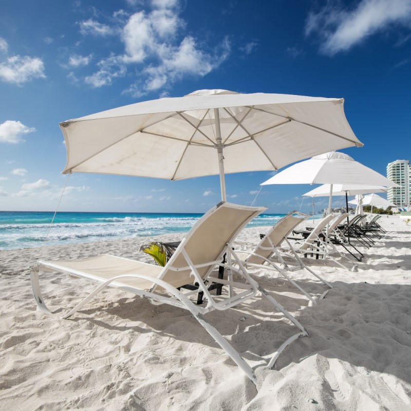 Beautiful Day in Cancun with white sand and blue water and lounge chairs with umbrellas on the beach.