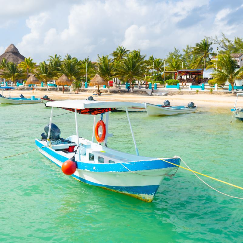Boat tied to dock in puerto morelos, mexico with blue waters and beach in background