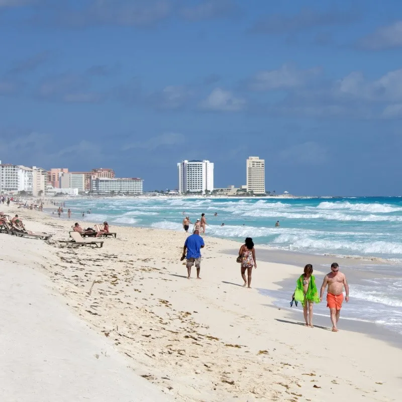 Cancun Beach with people walking in the sand and resorts in the distance.