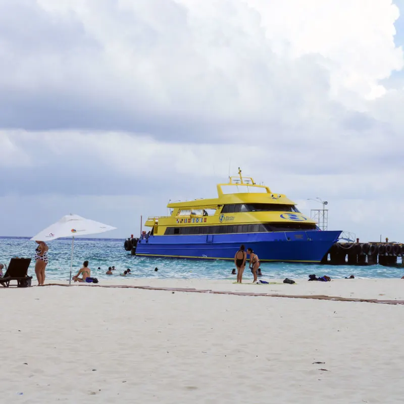 Ferry to Isla Mujeres from Cancun with tourists on the beach nearby.