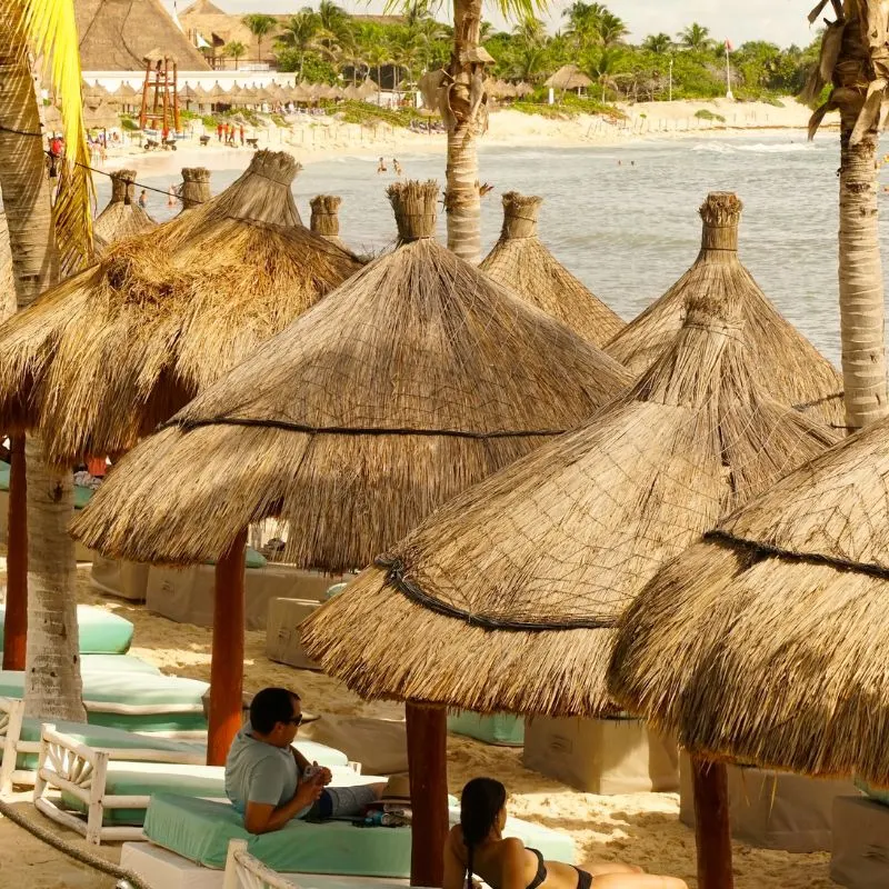 man and woman laying down on beach bed under tiki hut on a sunny day at cancun resort private beach
